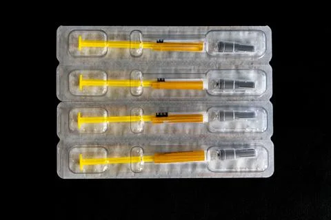 Four plastic syringes with yellow tips are stacked on top of each other Foto stock