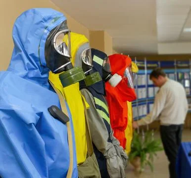 Four protective suits are displayed in a training center while a person obser Stock Photos
