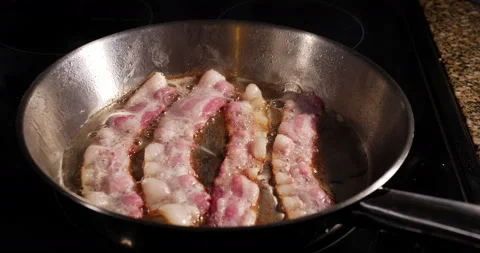 Four rashers of fatty bacon frying in hot oil in a pan Video stock 153751938