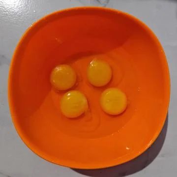 Four raw egg yolks separated into bright orange plastic mixing bowl Stock Photos