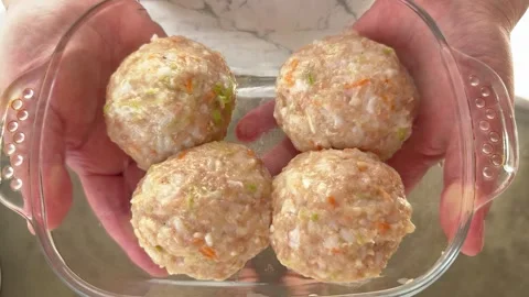 Four raw meatballs with rice and vegetables in a glass baking dish  Vídeo Stock 344782668