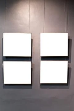 Four rectangular frames with white blank space hang on a grey wall by thin wi Stock Photos