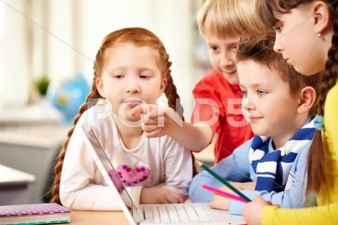 Four schoolchildren sitting at table and looking at laptop screen Stock Photos