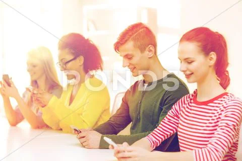 Four smiling students with smartphones at school Stock Photos