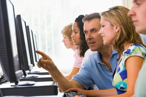 Four students sitting at computer terminals with teacher helping one of them Foto stock
