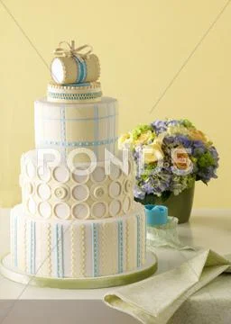 A Four-Tier Wedding Cake; Behind It, A Gorgeous Bouquet Of Summer Flowers