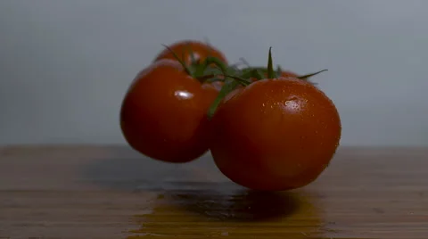 Four tomatoes connected on the vine are dropped onto a cutting board Stock Footage 64329150