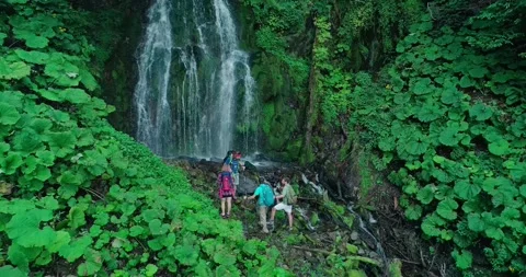 Four tourists looking to stream falling from great height with channel littered Stock Footage 209126744