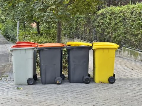 Four trash cans are lined up on the sidewalk Stock Photos
