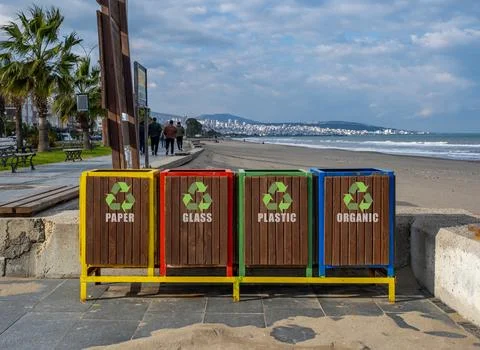 Four trash cans are lined up on a beach, each with a different colored lid 스톡 사진