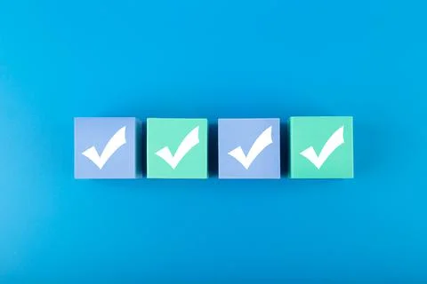 Four white checkmarks on multicolored cubes in a row against blue background Stock Photos