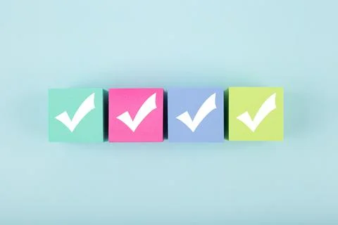 Four white checkmarks on multicolored cubes in a row against bright pastel blue Stock Photos