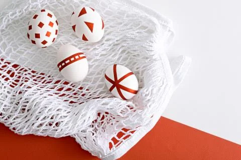 Four white Easter eggs with red geometric pattern on white mesh eco bag on re Stock Photos