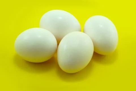 Four white eggs on yellow background, horizontal studio shot Stock Photos