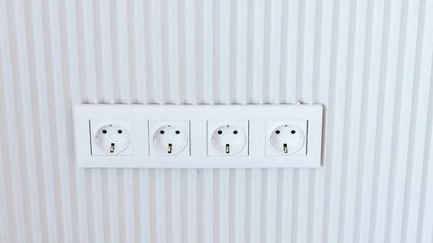 Four white electrical power outlets mounted on a textured white wall with v.. Stock Photos