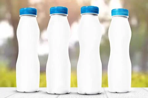Four white plastic bottles for dairy products on a gray wooden table against  Stock Photos