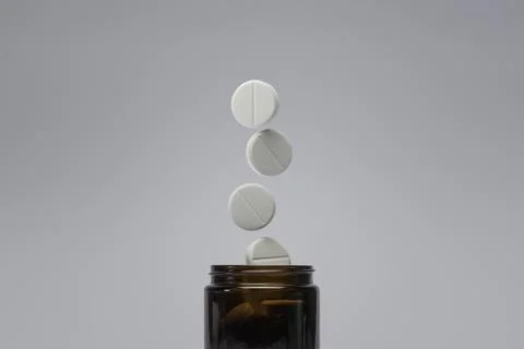 Four white tablets appear to float above a brown glass jar, symbolizing healt Stock Photos