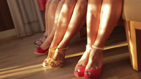 Four women cross their legs in sandals in the sun Stock Footage