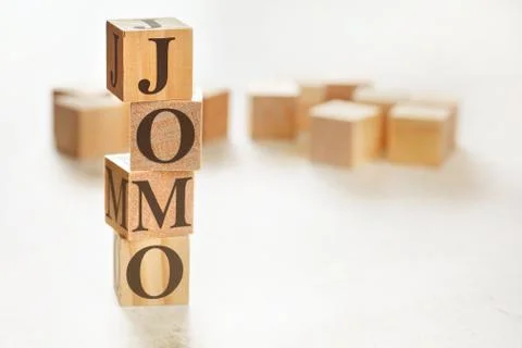Four wooden cubes arranged in stack with text JOMO meaning Joy of missing out on 스톡 사진