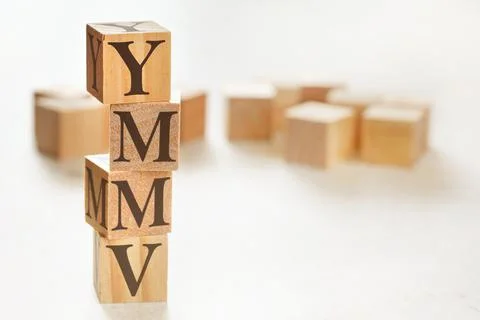 Four wooden cubes arranged in stack with letters YMMV (meaning Your mileage m 스톡 사진