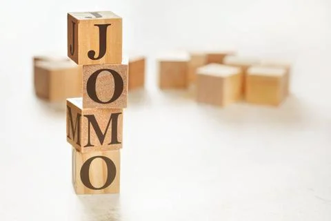 Four wooden cubes arranged in stack with text JOMO meaning Joy of missing ... 스톡 사진