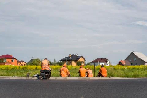 Four workers resting on the road construction site with a houses behind them. Stock Photos