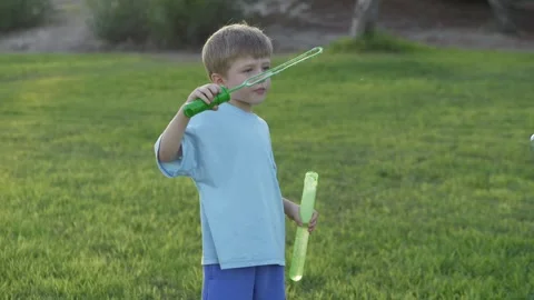 Four-year-old boy blows bubbles with joy on a sunny day surrounded by grass. The Stock Footage 317318851