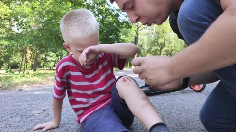 A four-year-old boy fell off a scooter and broke his knee. Dad provides first ai Video stock 136503077