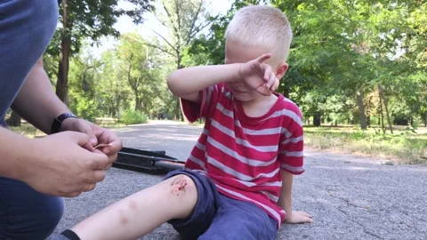 A four-year-old boy fell off a scooter and broke his knee. Dad provides first ai Stock Footage 136503113