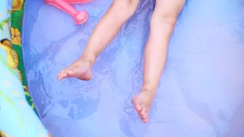 A four-year-old boy lies in a children's inflatable pool, splashing water Stock Footage 80441516