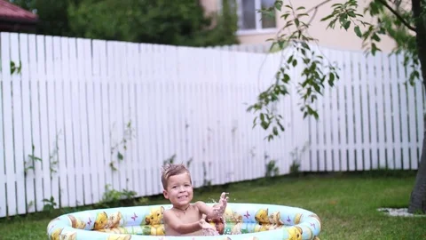 A four-year-old boy lies in a children's inflatable pool, splashing water Stock Footage 80441691
