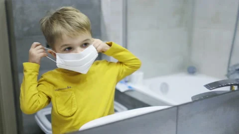 A four-year-old boy make funny faces and puts on a mask in front of a mirror Stock Footage 169248051