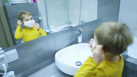 A four-year-old boy puts on a mask in the bathroom in front of a mirror Stock Footage 169247931