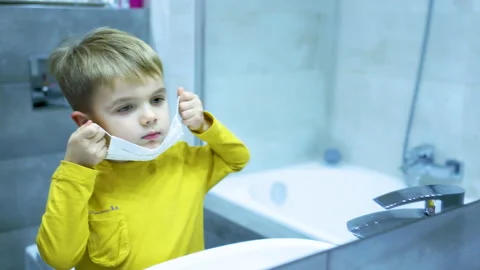 A four-year-old boy puts on a mask in the bathroom in front of a mirror Stock Footage 169248262