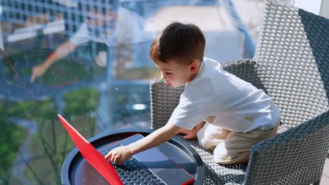 Four-year-old boy in white t-shirt sits at the window on sunny day. Stock Footage 320948444