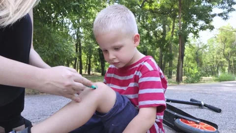 A four-year-old child fell off a scooter and injured his knee. Mom dabs the woun Stock Footage 136503187