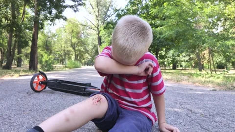 A four-year-old child fell off a scooter and injured his knee. The child cries,  Stock Footage 136503265
