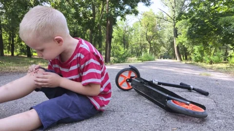 A four-year-old child fell off a scooter and injured his knee. The child cries,  Stock-Footage 136503306