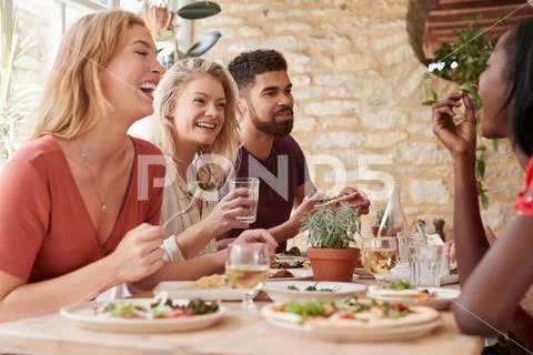 Four young adult friends eating in a restaurant, close up Stock Photos