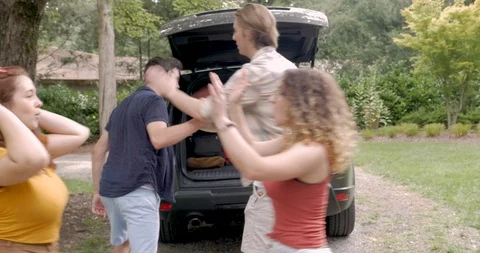 Four young adults high five and get into an SUV getting ready for a road trip Stock Footage 122103107