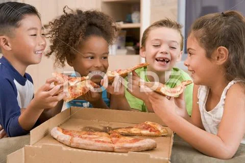 Four young children indoors eating pizza smiling Stock Photos