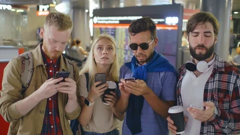 Four young friends checking their flight information using smartphones. Stock Footage 121830240