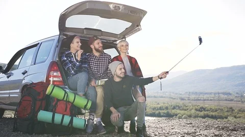 Four of young people doing selfie on smartphone, sitting leaning on trunk of suv Stock Footage 102978932