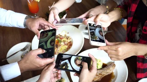 Four young people using a mobile phone and taking photos of food at restaurant Stock Footage 92957449