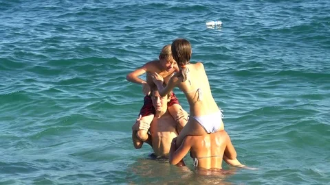 Four youngs playing on the beach standing chest high in the water laughing Vidéo 79861514