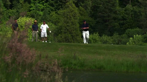 Foursome at water hazard, one golfer hitting ball into water Stock Footage 59519306