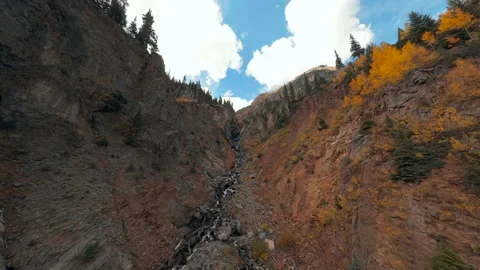 FPV Aerial flying up a mountain stream with waterfalls and fall foliage Stock Footage 162326850