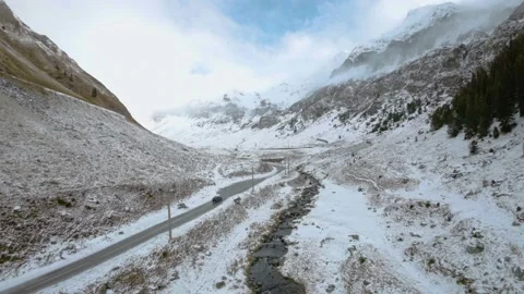 FPV Aerial view of car driving down on a frozen mountain road covered with snow Stock Footage 224733896