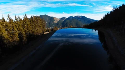 FPV dive down an autumn forest towards clear lake reflecting blue sky mountains Stock Footage 296582166
