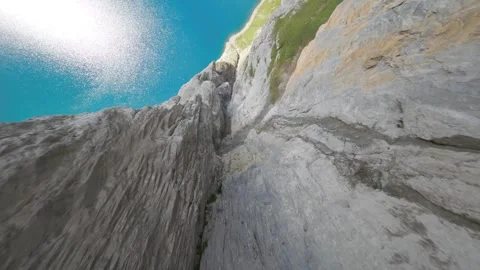 An FPV drone diving down along a cliff above a high-altitude lake in Switzerland Stock Footage 253553699